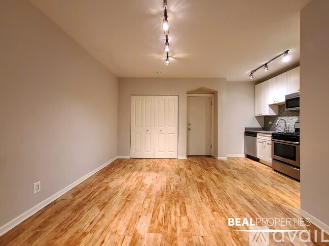 A spacious room with wooden flooring and a kitchen area in the background.