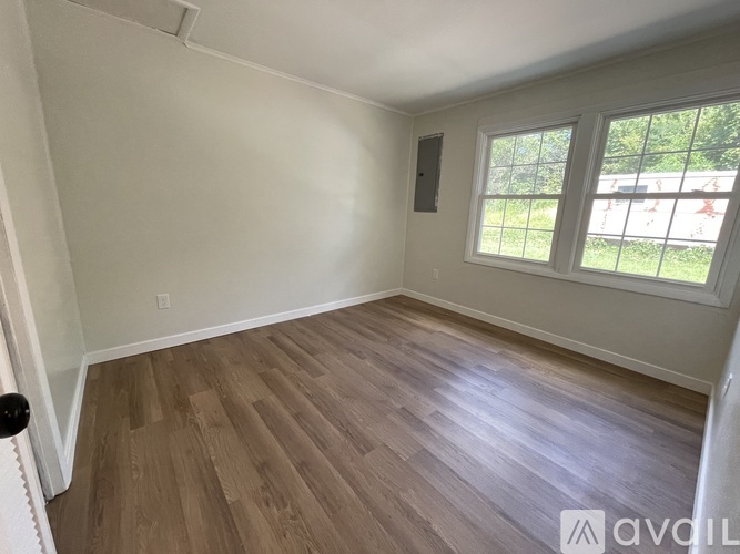 A room with wooden flooring and a window overlooking a green area.