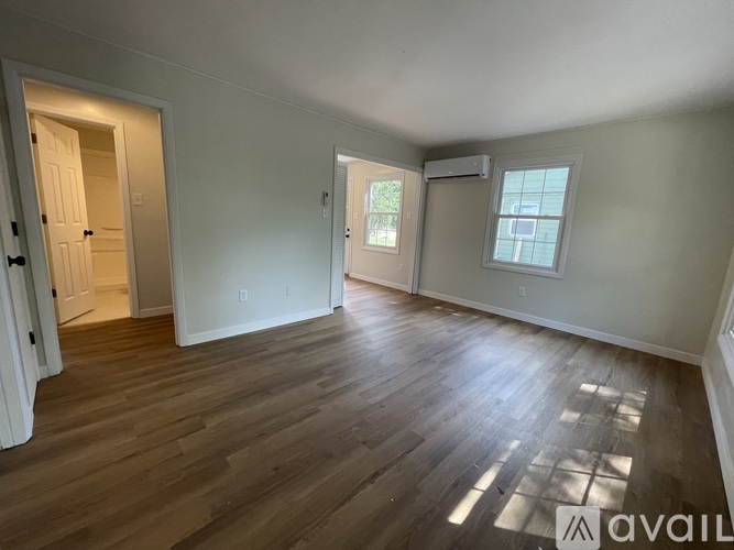 A room with wooden flooring and two windows.