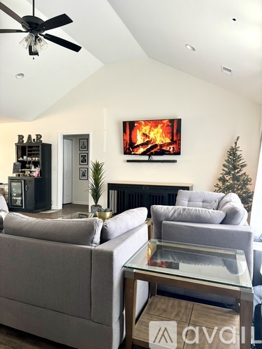A living room with a grey couch and a television displaying a fireplace.