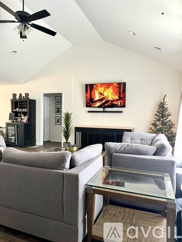 A living room with a grey couch and a television displaying a fireplace.