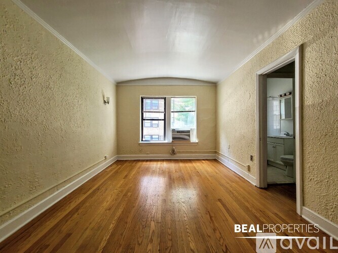 A room with wooden floors and a window with a view of trees.