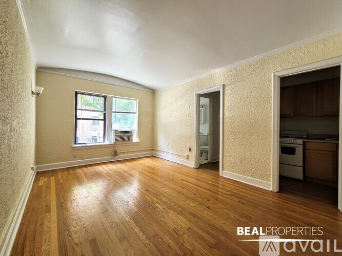 A room with wooden floors and a window with a view of trees and buildings outside.