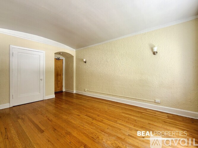 A room with wooden floors and white walls, with a door on the left and a small light fixture on the wall.