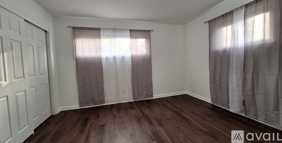 A room with wooden floors and two windows with curtains.