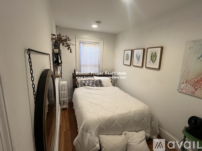 A bedroom with a white bed and a window with blinds.