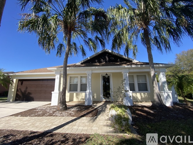 A house with a brown roof and a white garage door is surrounded by palm trees.