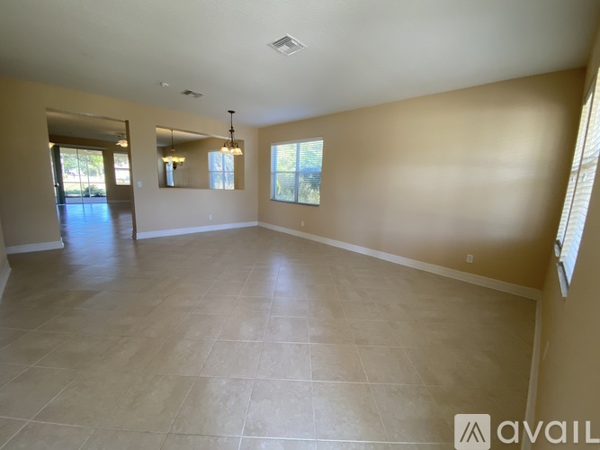 A spacious room with beige walls and flooring, a chandelier, and a large window.