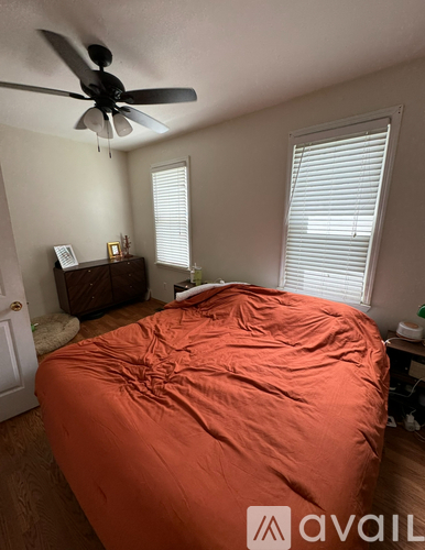 A bedroom with a bed covered in an orange sheet and a ceiling fan.