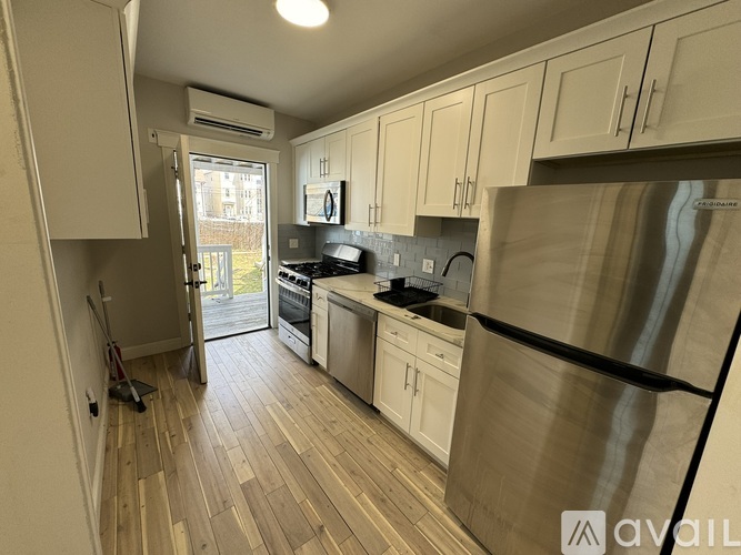 A kitchen with a stainless steel refrigerator, wooden flooring, and white cabinets.