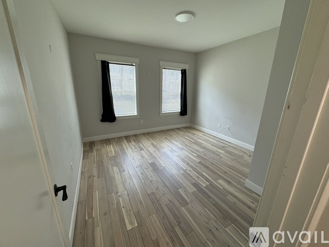 A room with wooden flooring and two windows.