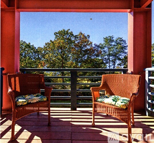 Two wicker chairs with cushions are on a porch with a view of trees.
