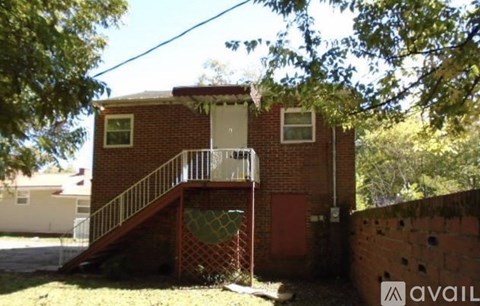 A house with a red brick exterior and a white door is surrounded by trees.