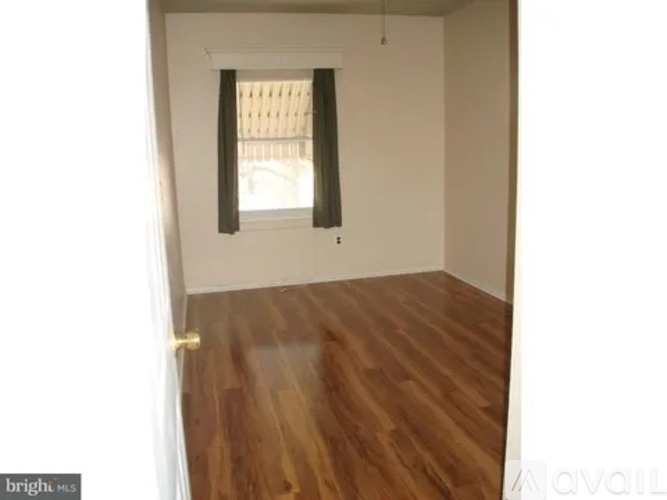 A room with wooden flooring and a window with a green curtain.