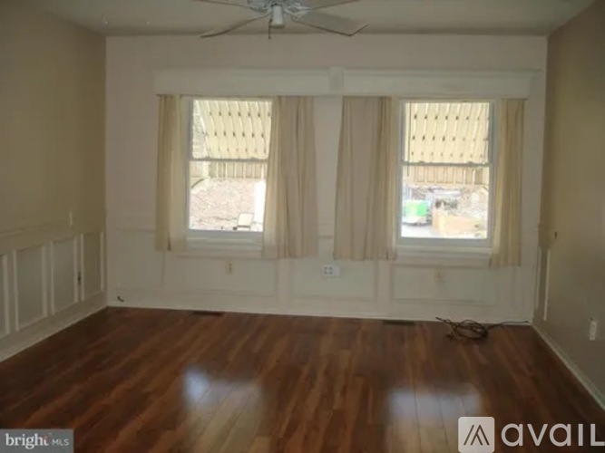 A room with wooden floors and two windows covered with curtains.