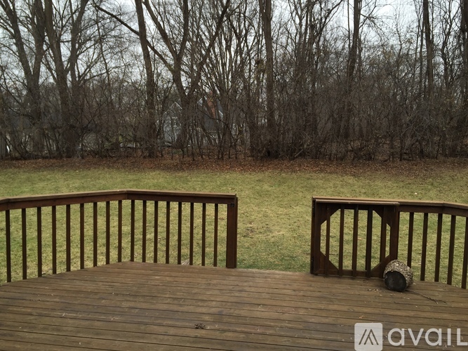 A wooden deck with a railing and a view of a grassy field and trees.