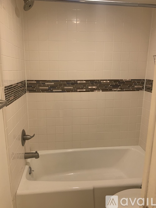 A white bathtub with a black and white tile strip above it.
