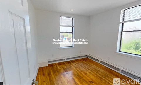 A room with wooden flooring and two windows, one of which has a view of a tree.