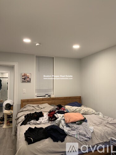 A bedroom with a bed covered in clothes and a sign that says "Boston Popper Real Estate".