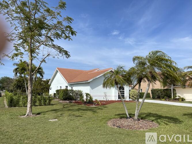 A house with a red roof and white walls is surrounded by greenery.