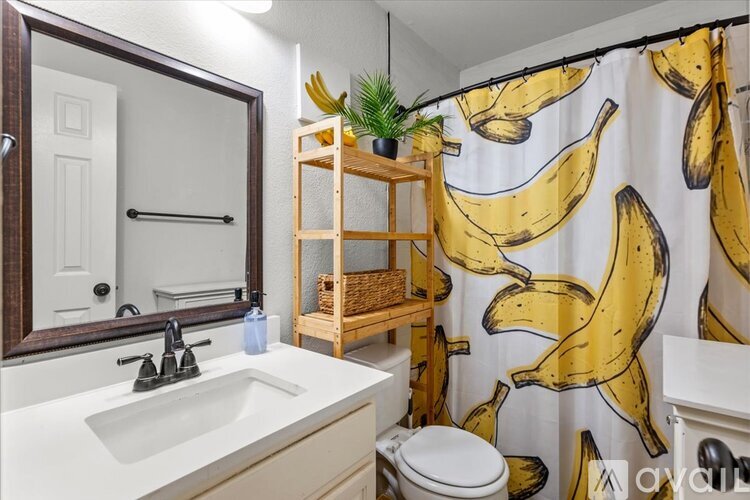 A bathroom with a banana shower curtain and a wooden shelf.