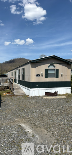 A mobile home sits on a gravel lot with a mountain in the background.