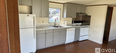 A kitchen with white appliances and a wooden floor.