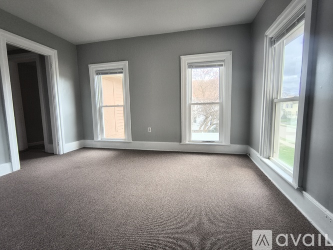 A room with grey walls and carpeted floor with three windows.