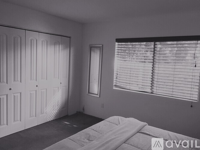A bedroom with a bed, a window with blinds, and a wall-mounted mirror.