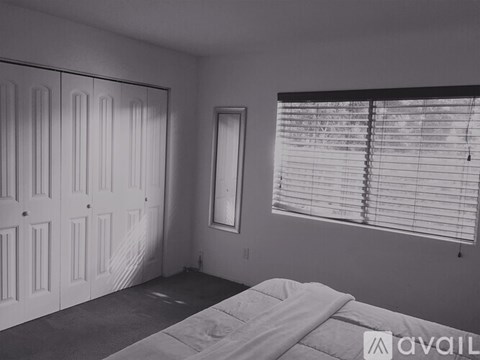 A bedroom with a bed, a window with blinds, and a wall-mounted mirror.