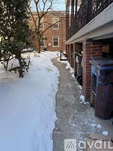 A snow-covered pathway leads to a brick building with a blue dumpster on the right.