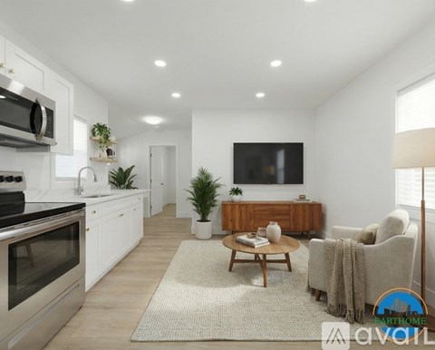 A modern kitchen with a stainless steel oven and microwave, a wooden coffee table, a couch, and a flat-screen TV mounted on the wall.