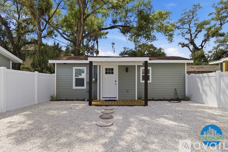 A small house with a white fence and a gravel driveway.