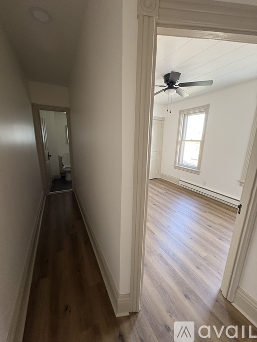 A hallway with wood floors and white walls leading to a bedroom.