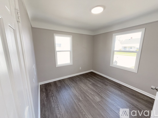 A room with wooden flooring and two windows.