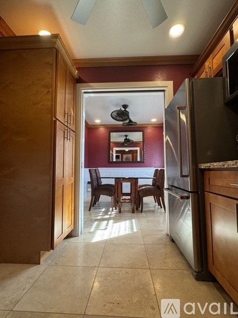A kitchen with a refrigerator, a dining table with chairs, and a ceiling fan.