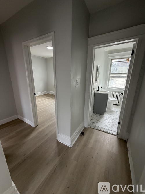 A room with a wooden floor and white walls, with a doorway leading to another room.