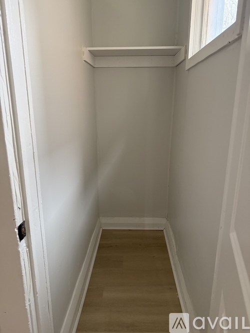 A white hallway with a wooden floor and a door on the left.