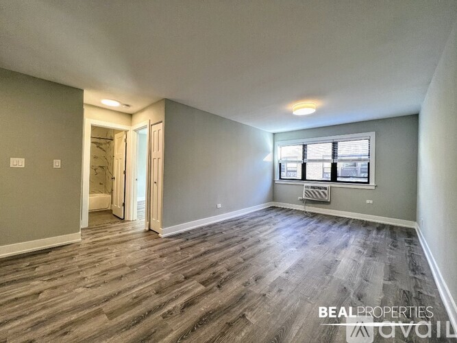 A spacious room with wooden flooring and a window with blinds.