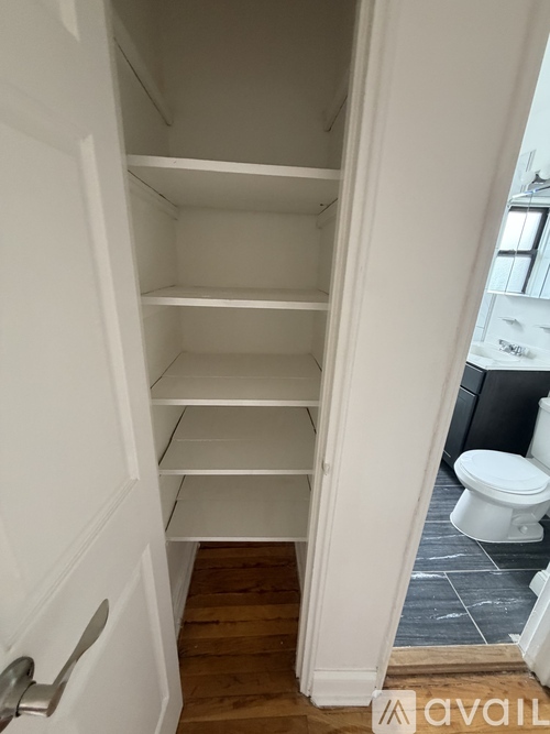A white door with a silver handle is open to a hallway with a toilet in the background.