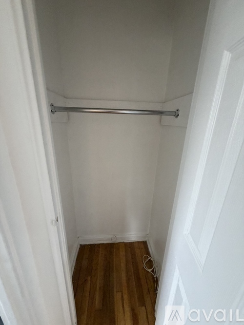 A white closet with a wooden floor and a metal rod.