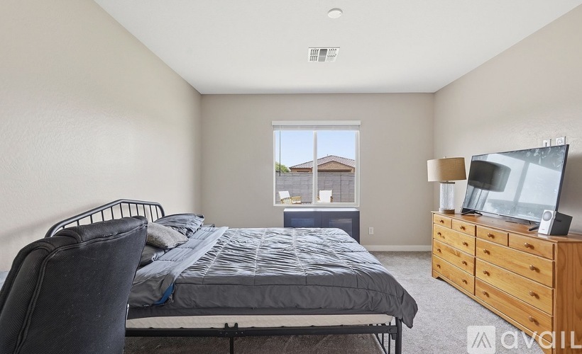 A bedroom with a bed, chair, and dresser with a flat screen TV on top.