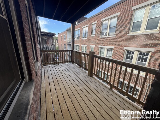 A balcony with wooden flooring and brick buildings in the background.