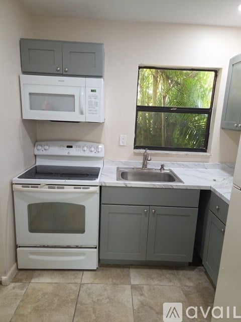 A kitchen with a white oven and microwave, a white sink, and a window with a view of trees.