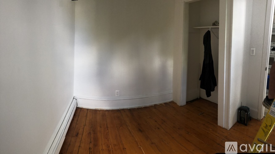 A room with a wooden floor and a white wall with a coat hanging on it.