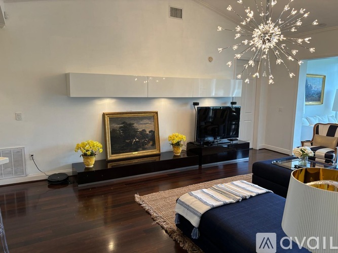 A living room with a large painting, a flat screen TV, and a chandelier.