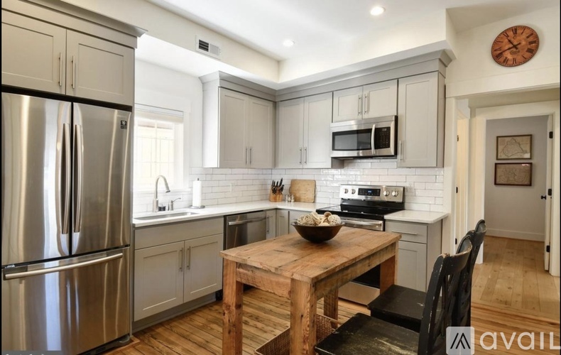 A kitchen with a wooden table and chairs, a refrigerator, a microwave, and a clock on the wall.