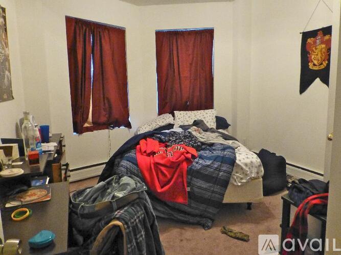 A bedroom with a bed covered in clothes and a Harry Potter flag on the wall.