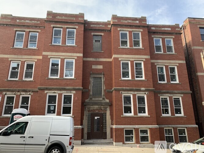 A white van is parked in front of a red brick building.