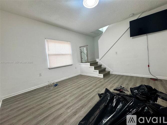 A room with wooden flooring and a staircase in the background.